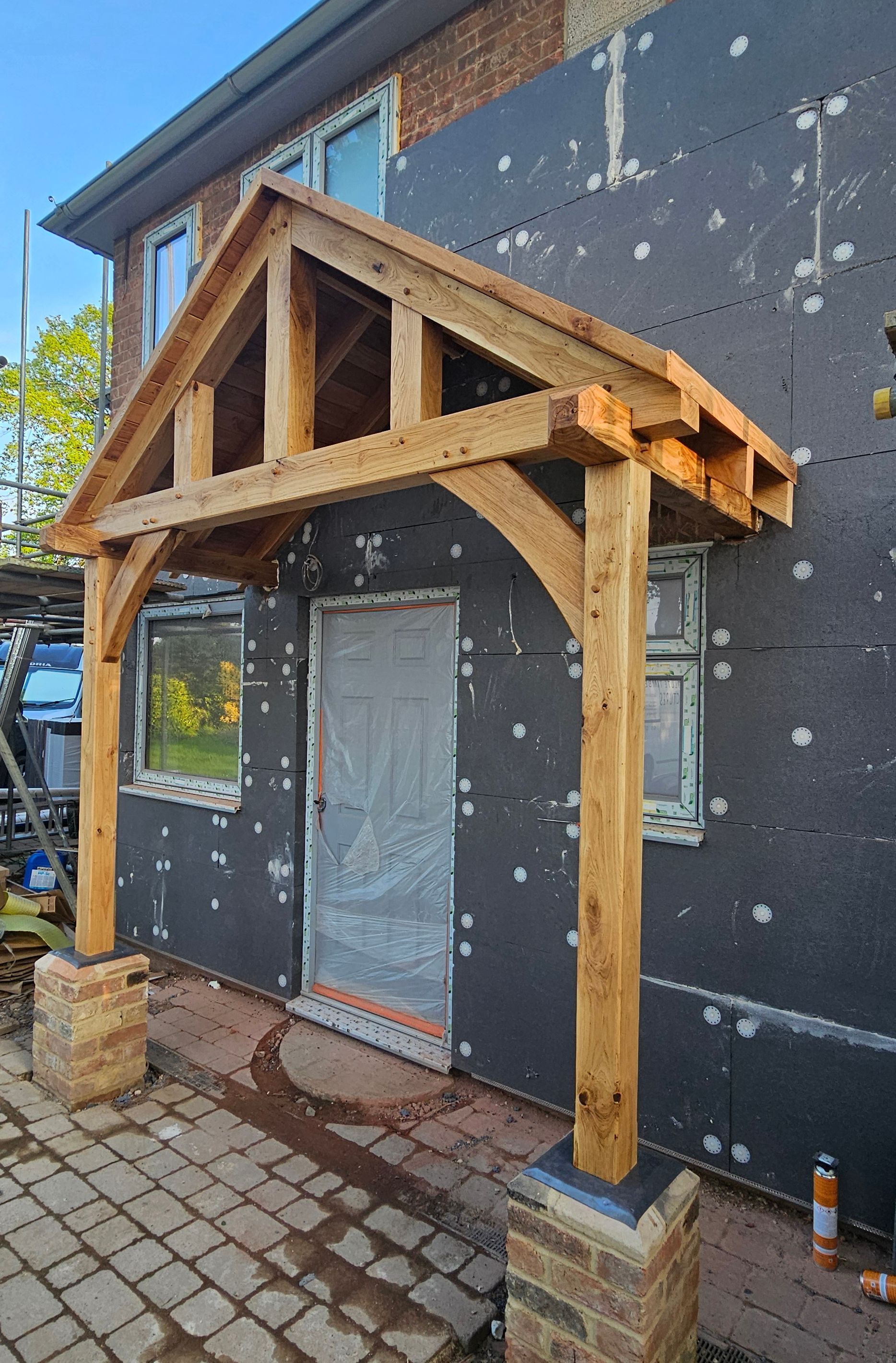 A new wooden porch frame under construction, mounted on brick pillars over a door on an unfinished building exterior.
