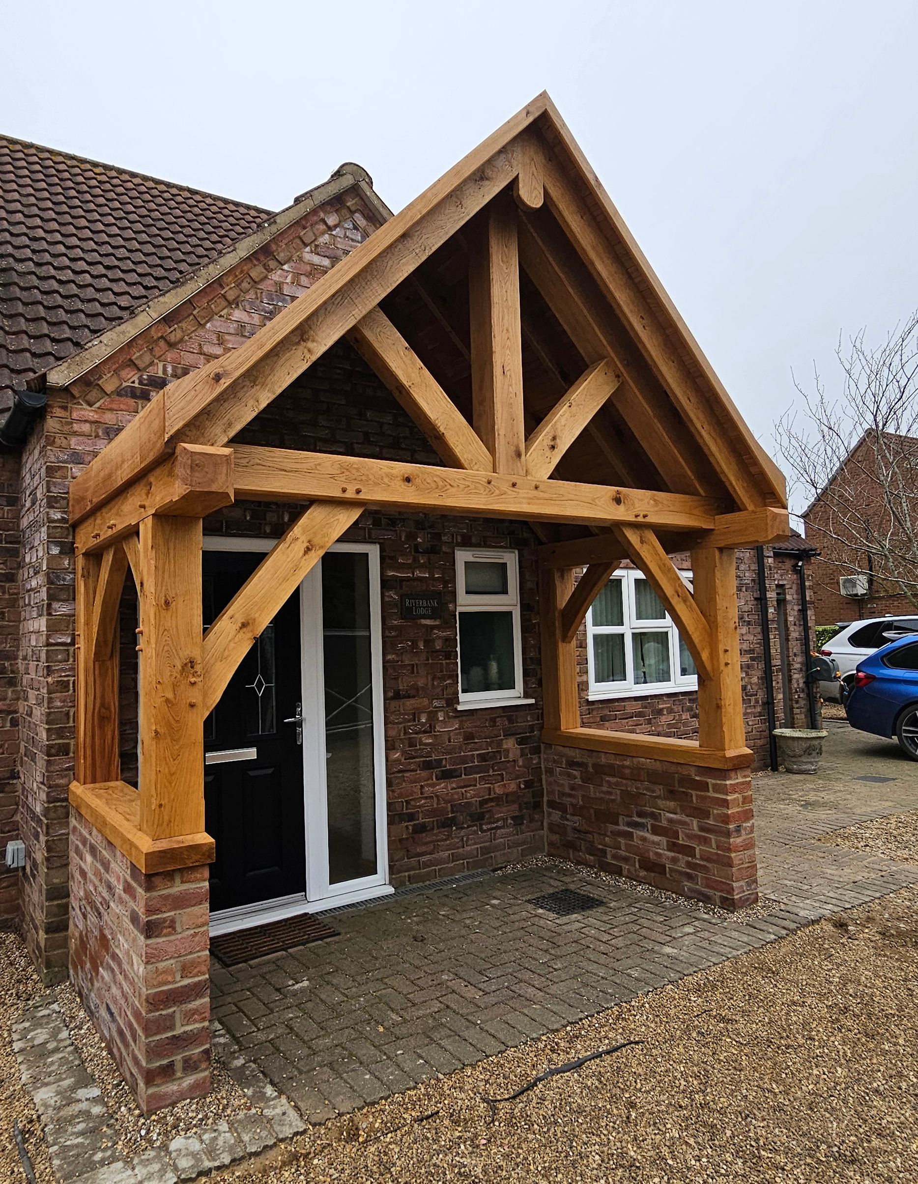 A rustic, timber-framed gabled porch extension over the entrance of a brick house with a dark front door.