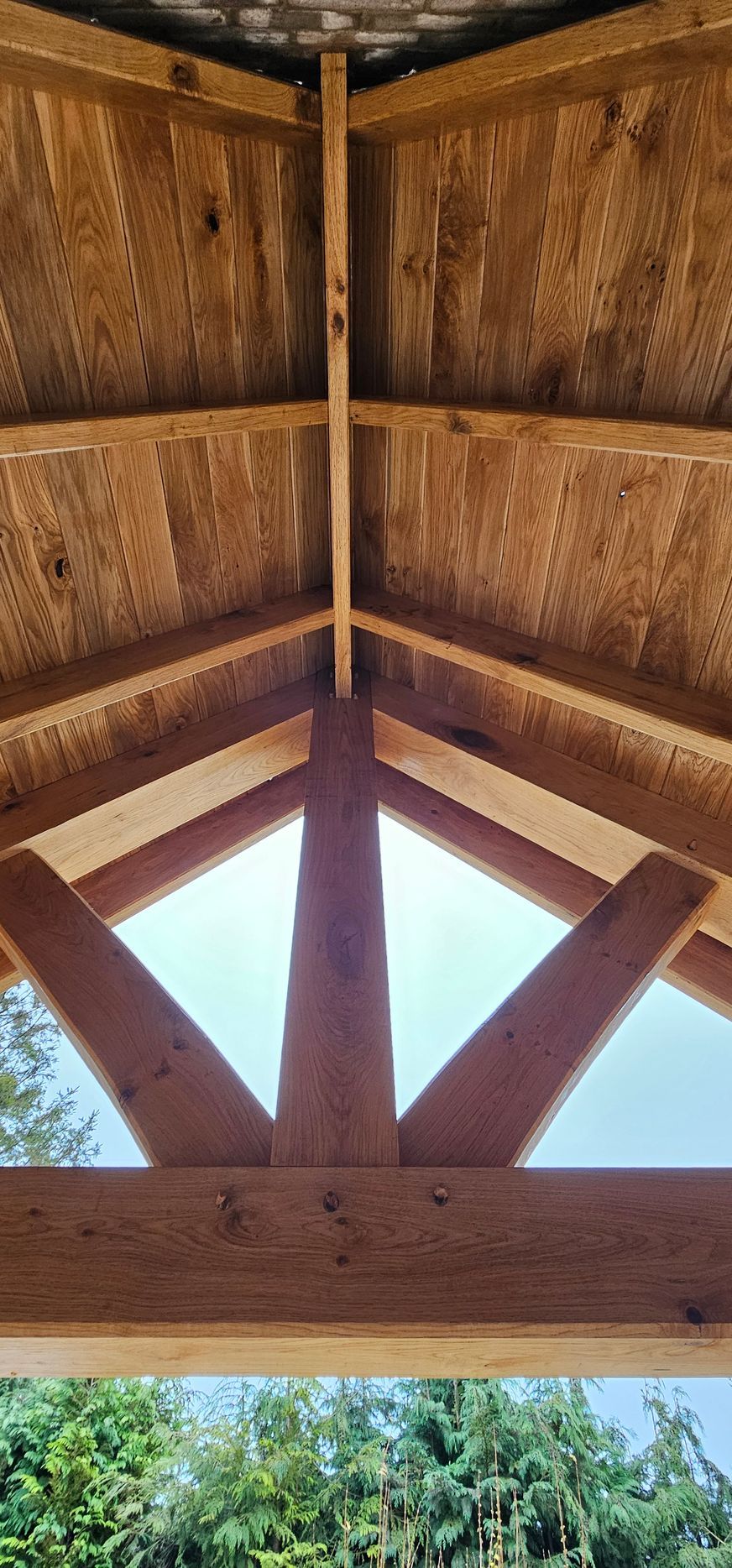 A low-angle view of a wooden porch roof structure with exposed rafters and beams against a bright, clear sky.