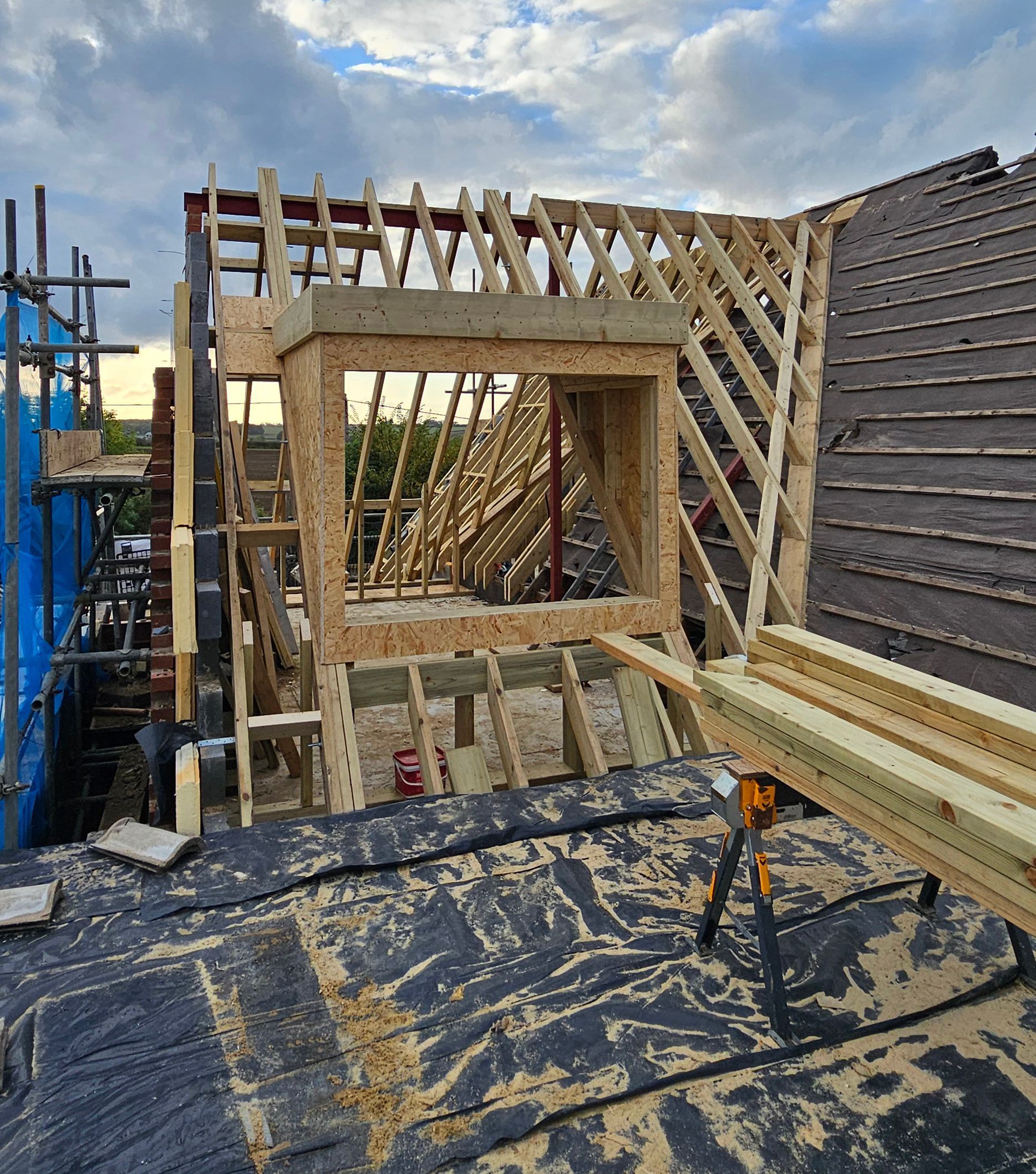 An exterior view of a residential building under construction, showing hand cut timber roof framing and a newly installed dormer.