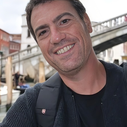 A man wearing a black sweater and a black backpack smiles for the camera