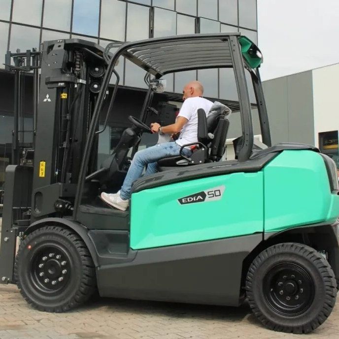 Uomo alla guida di un carrello elevatore verde acqua e nero all'aperto.