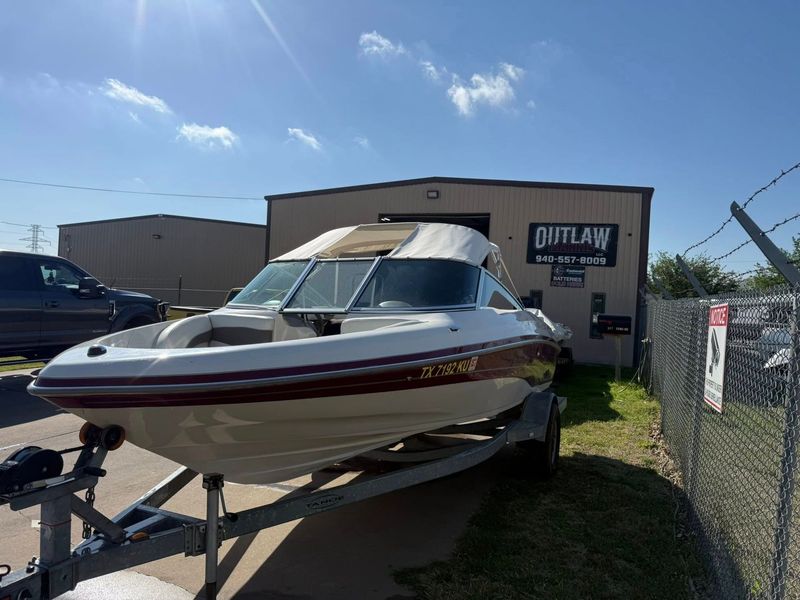 White speedboat on a trailer outside a building under a sunny blue sky.