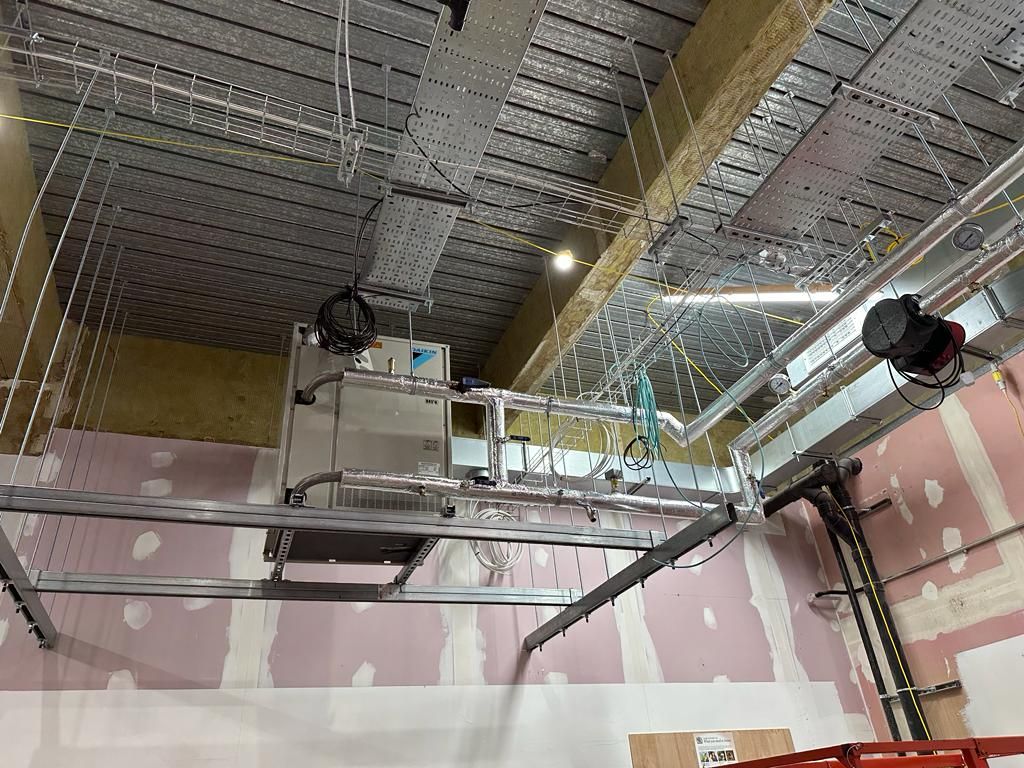 A ceiling with a lot of pipes and wires hanging from it.