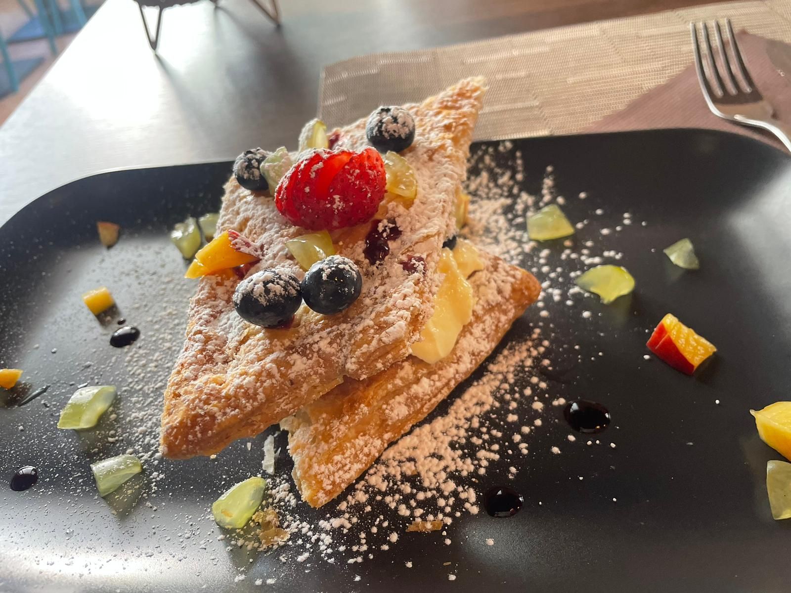 Un dessert con zucchero a velo e frutta su un piatto nero