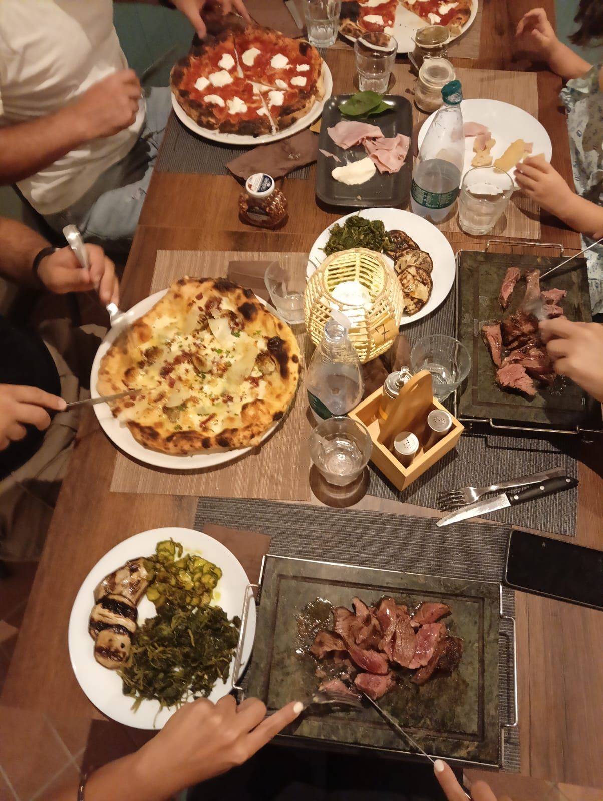 Un gruppo di persone è seduto a un tavolo e mangia pizza e carne