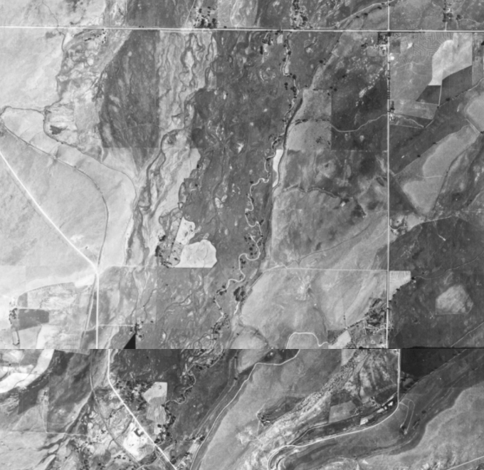Aerial grayscale view of a river cutting through a landscape with fields and hills.