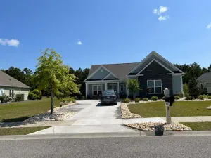 House with a driveway, blue siding, and brick-like accents. A car sits in the driveway, sunny day.