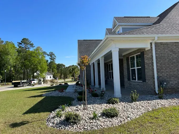 Brick house with white pillars and rock landscaping on a sunny day.