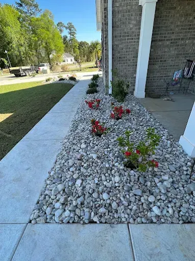 Concrete walkway beside a house with a rock garden and colorful flowers.