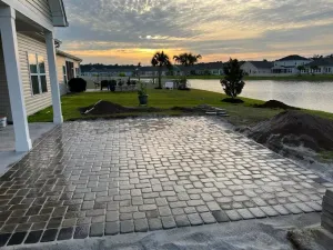 Brick patio next to a house overlooking a lake at sunset.