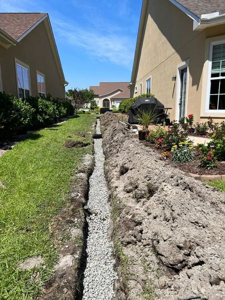 Long trench filled with gravel between two houses, for drainage.