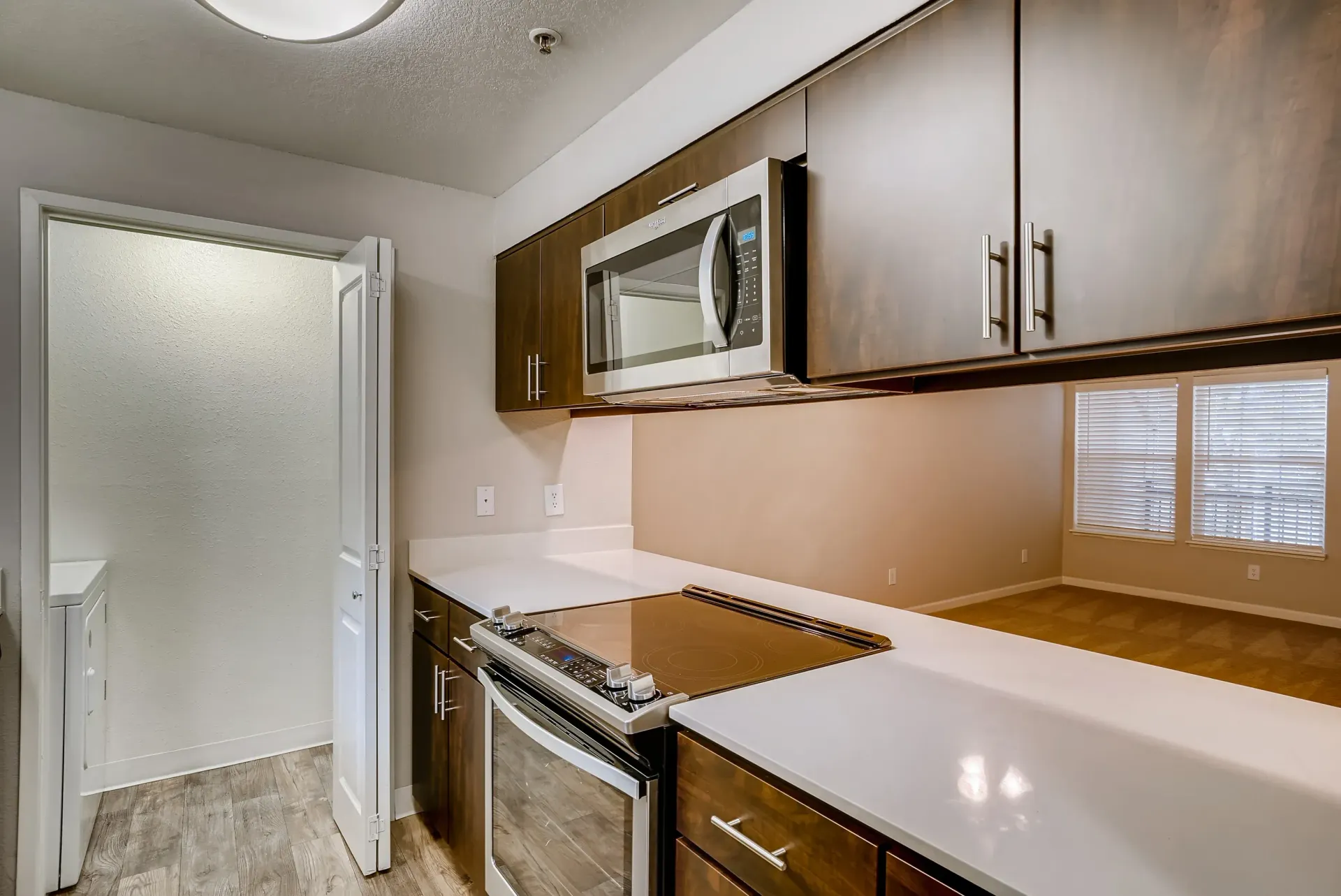 Kitchen in a modern apartment with dark wood cabinets, white countertops, and stainless appliances.