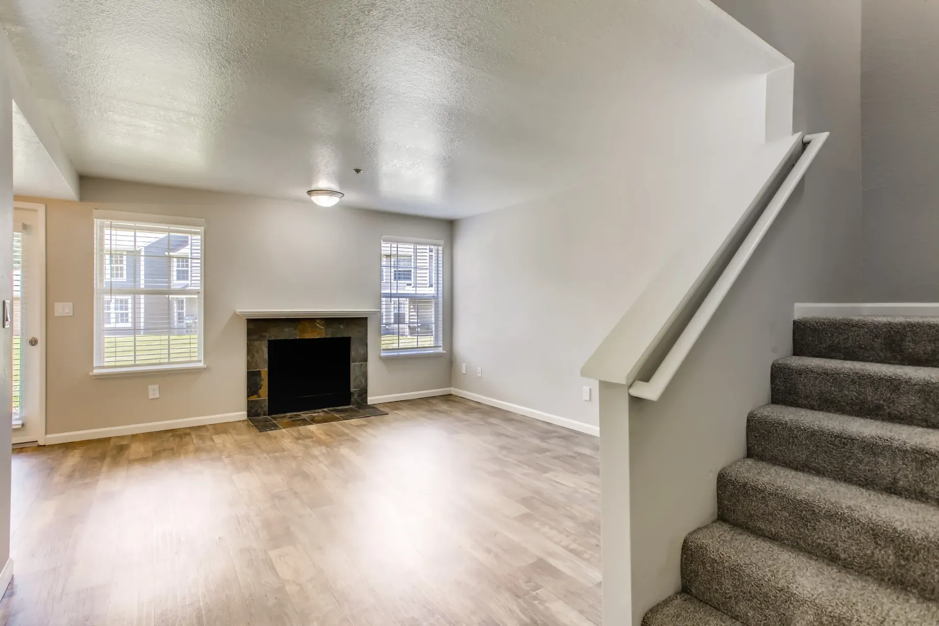 Open-concept living room with a fireplace, staircase, and two windows.