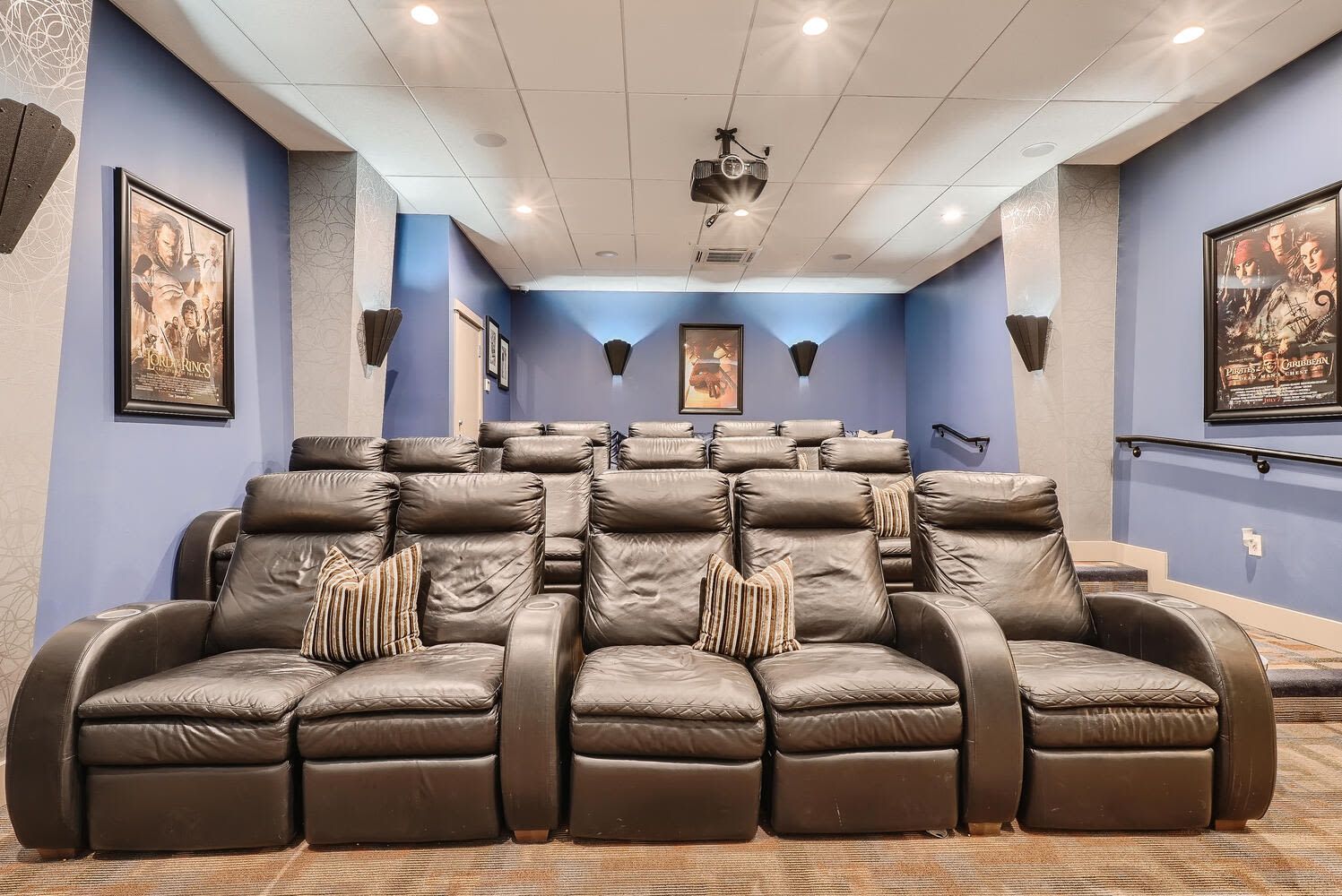 Theater-style community lounge with rows of black leather recliners and movie posters.