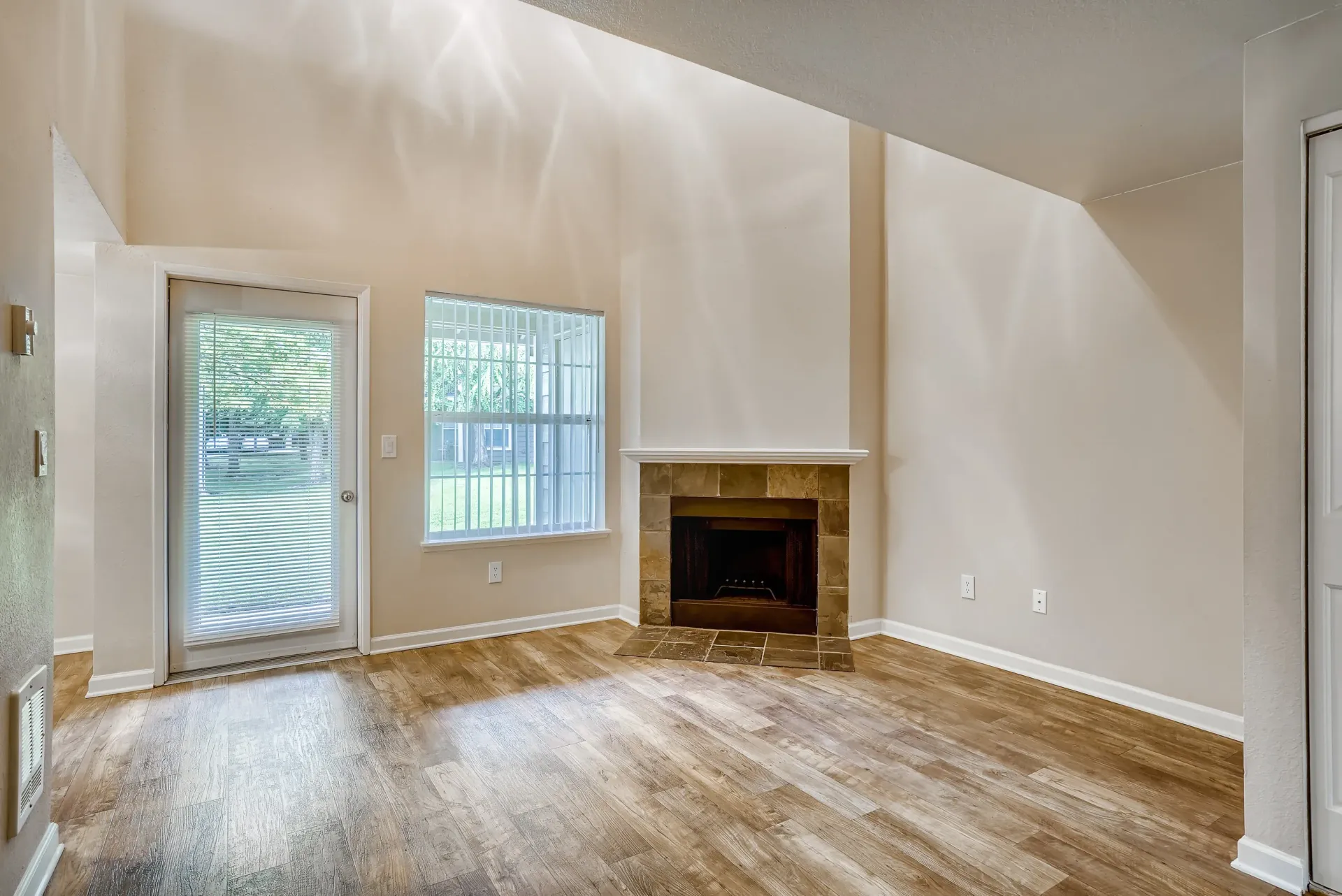 Living room with beige walls, wood-look flooring, a tile fireplace, and a glass door to the outside.