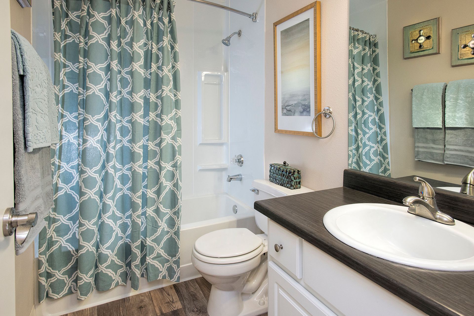 Bathroom in an apartment with teal patterned shower curtain, tub, toilet, and dark vanity.