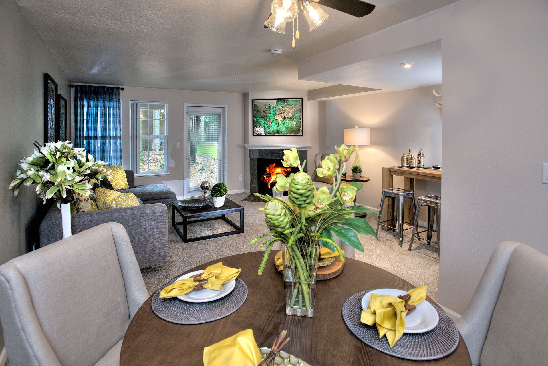 Furnished living room with fireplace, sofa, dining table, and large windows.