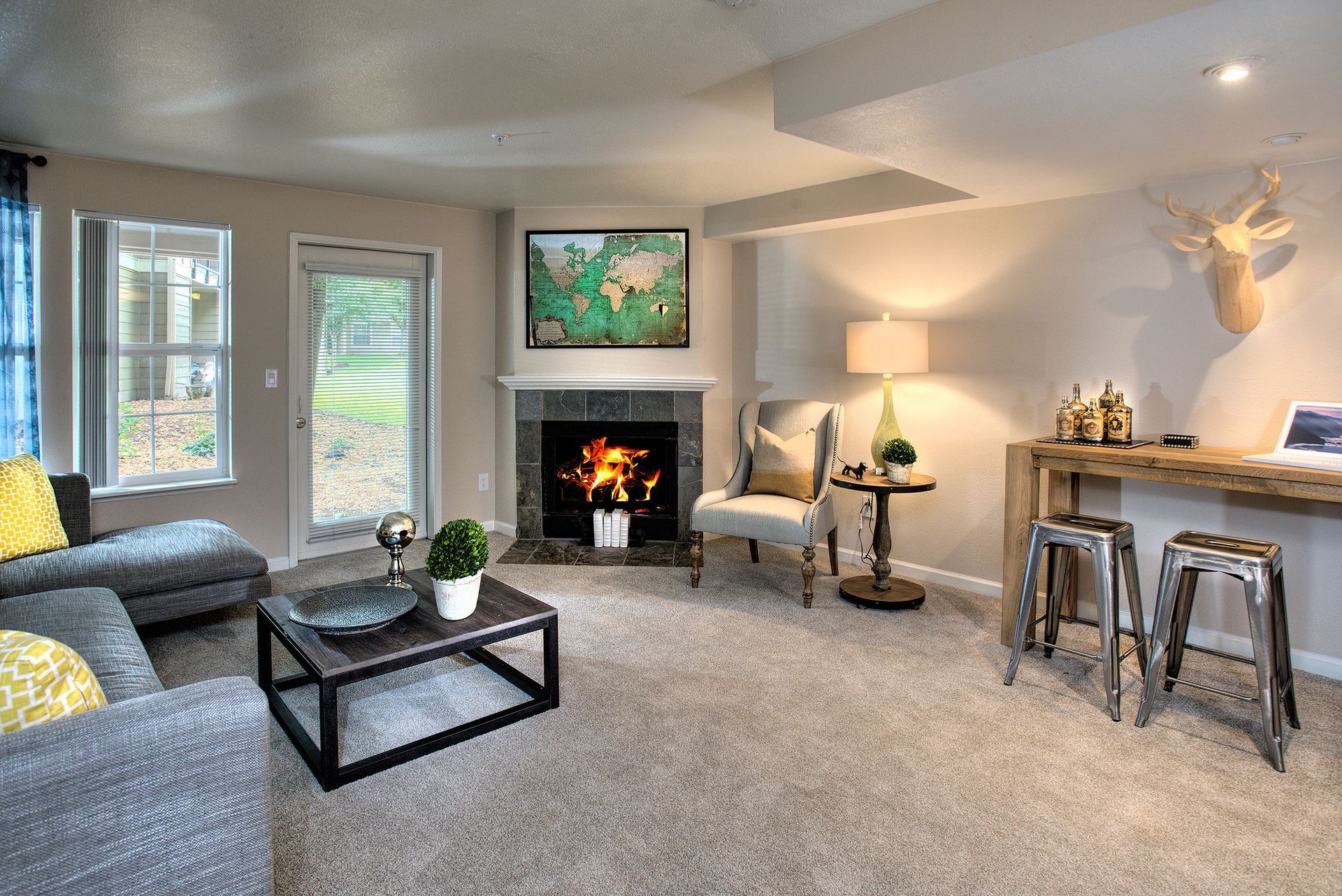 Living room in an apartment: beige walls, gray sectional sofa, fireplace, and a bar counter with stools.