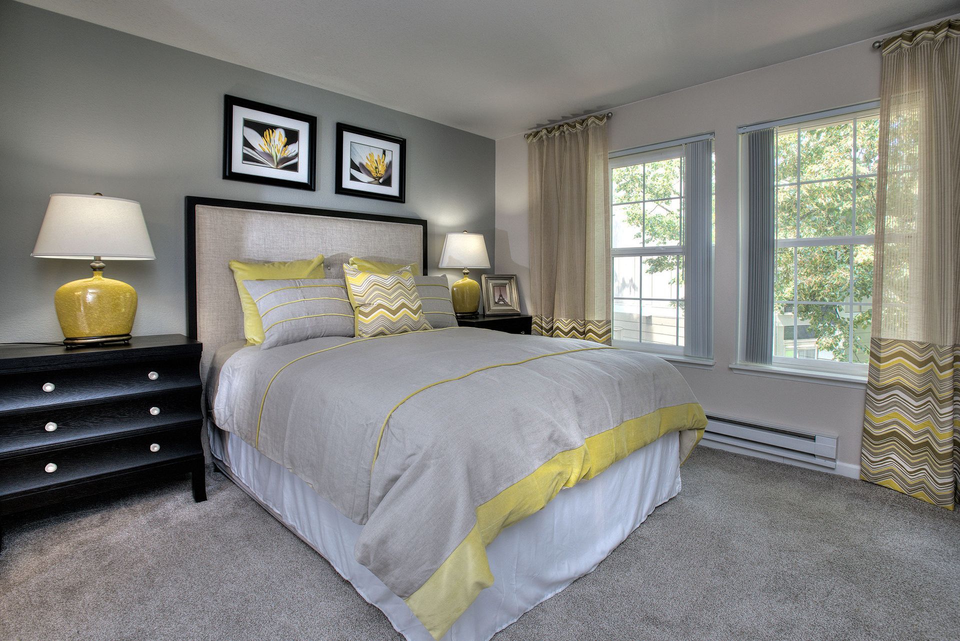 Bedroom in an apartment with a large bed, two nightstands, lamps, and two windows.