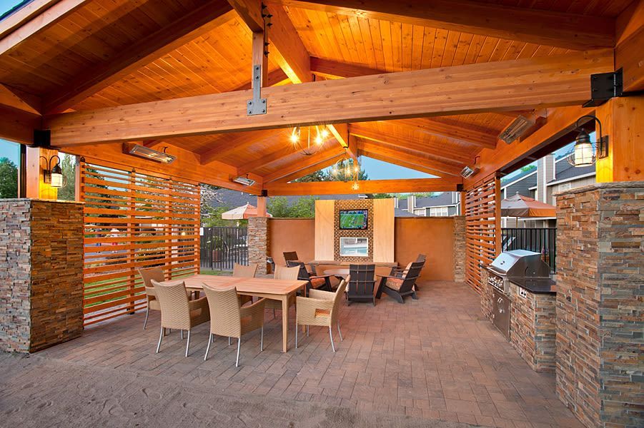 Covered outdoor communal lounge with a large dining table, chairs, grills, and stone pillars.