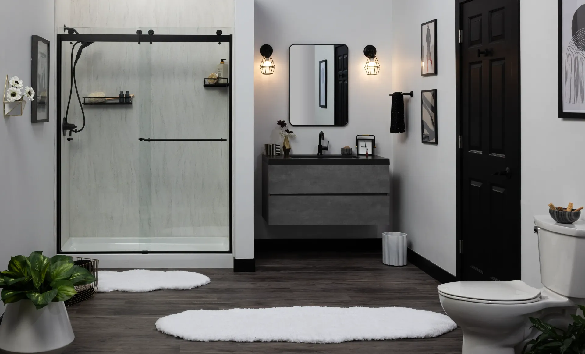 Modern gray bathroom with walk-in shower, vanity, black door, and white bath mats