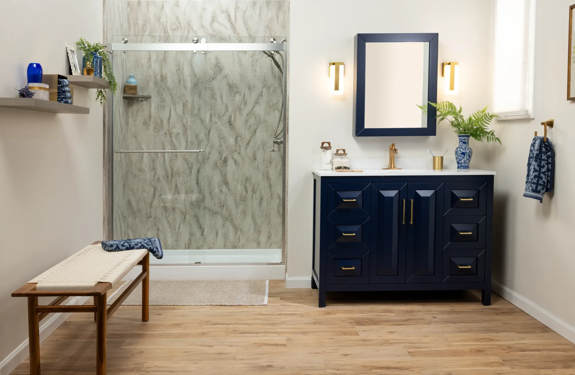 Modern bathroom with navy vanity, marble shower, wall mirror, bench, and wood floor.