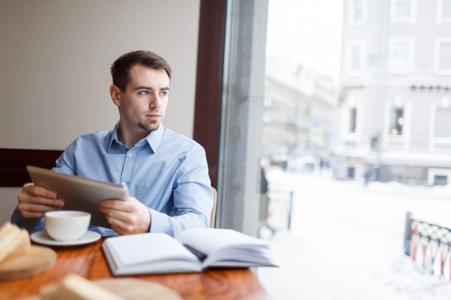 A man is sitting at a table with a cup of coffee and a tablet.