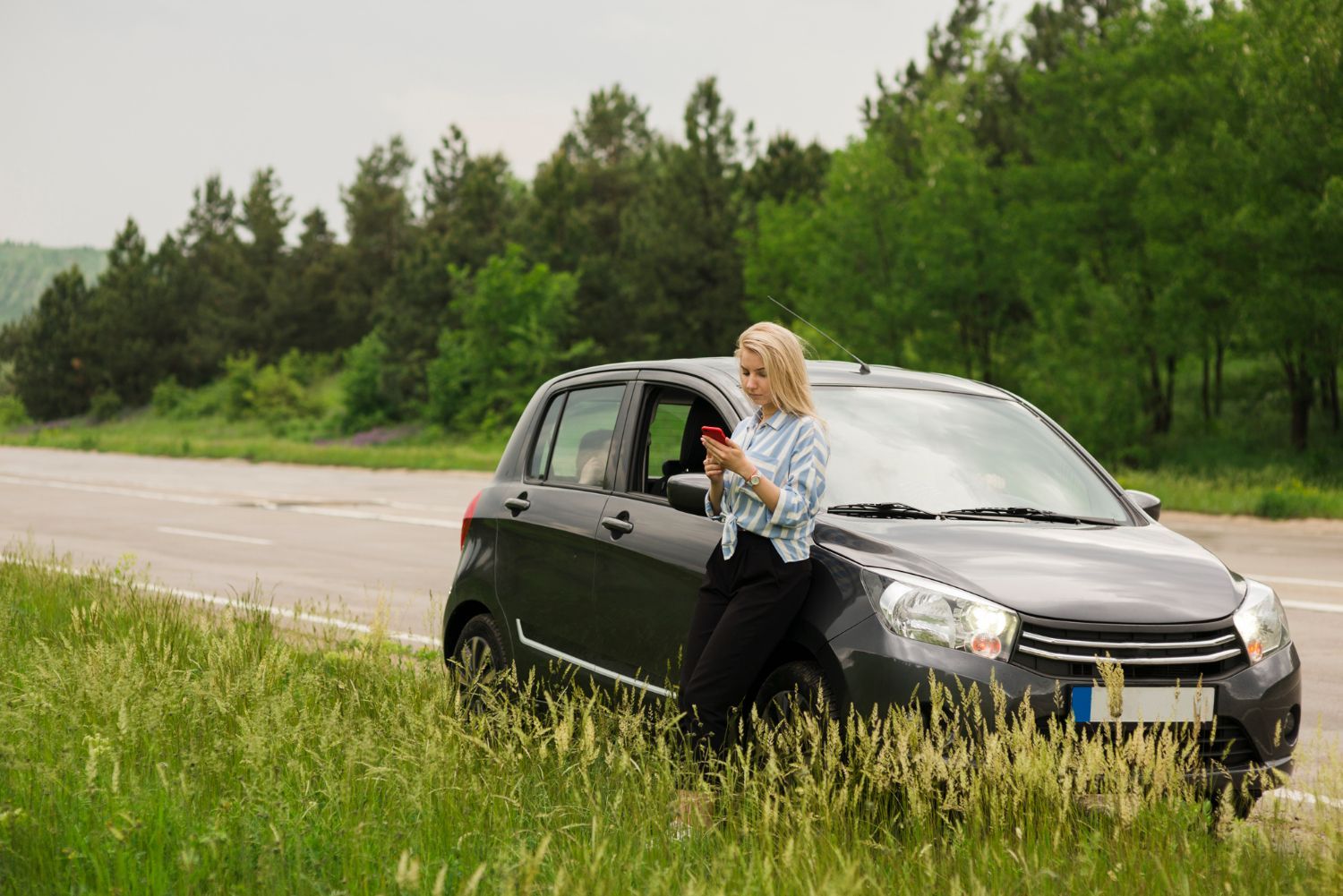 A woman is standing next to a broken down car on the side of the road.