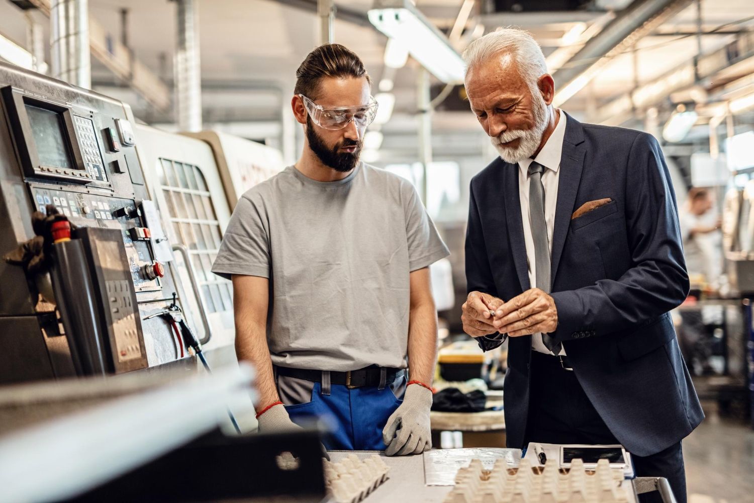 A man in a suit and tie is talking to a man in a factory.