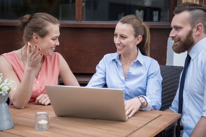 A man and two women are sitting at a table with a laptop.