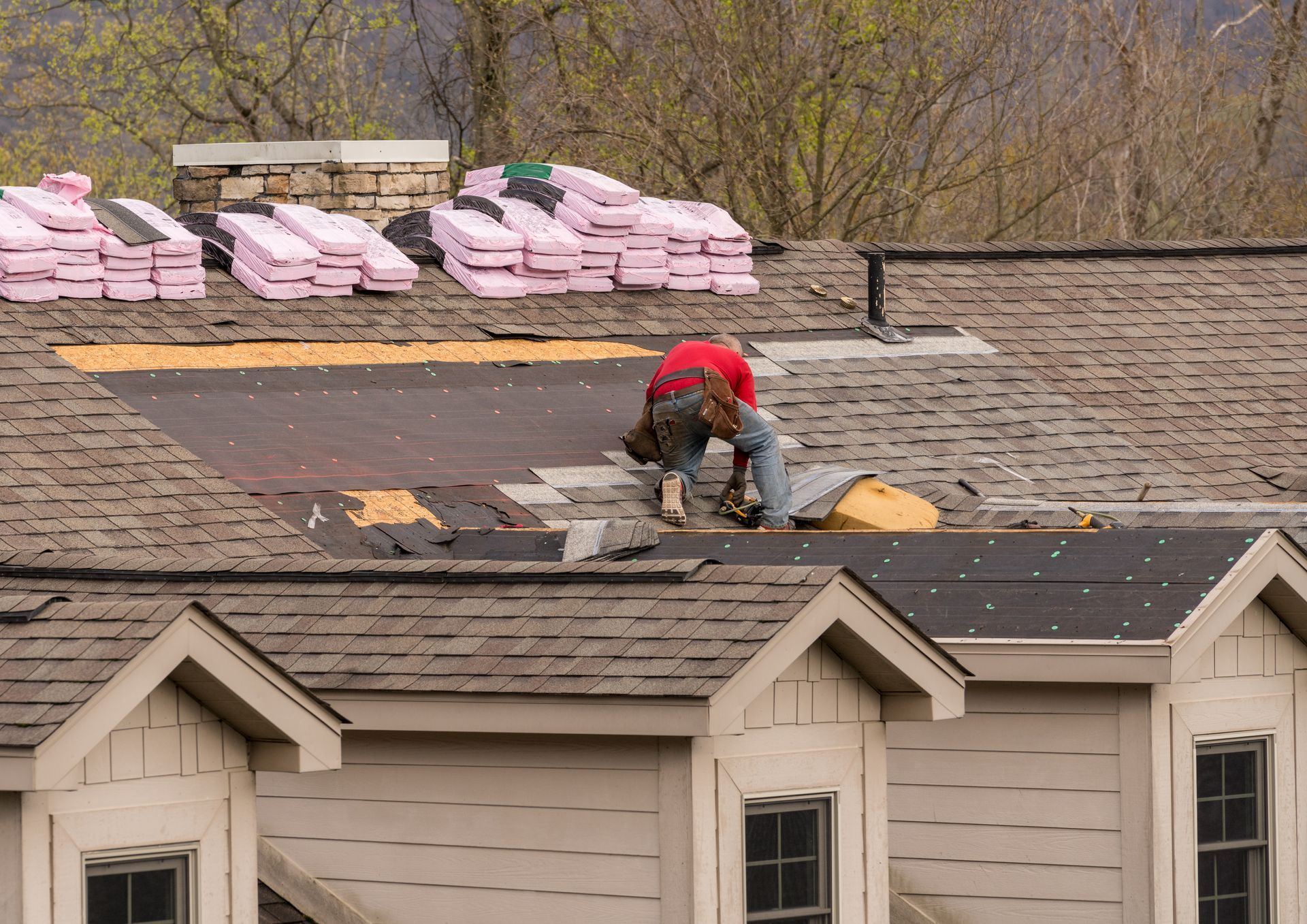 Roofer in red shirt working on a house roof. Pink insulation and other roofing materials visible.