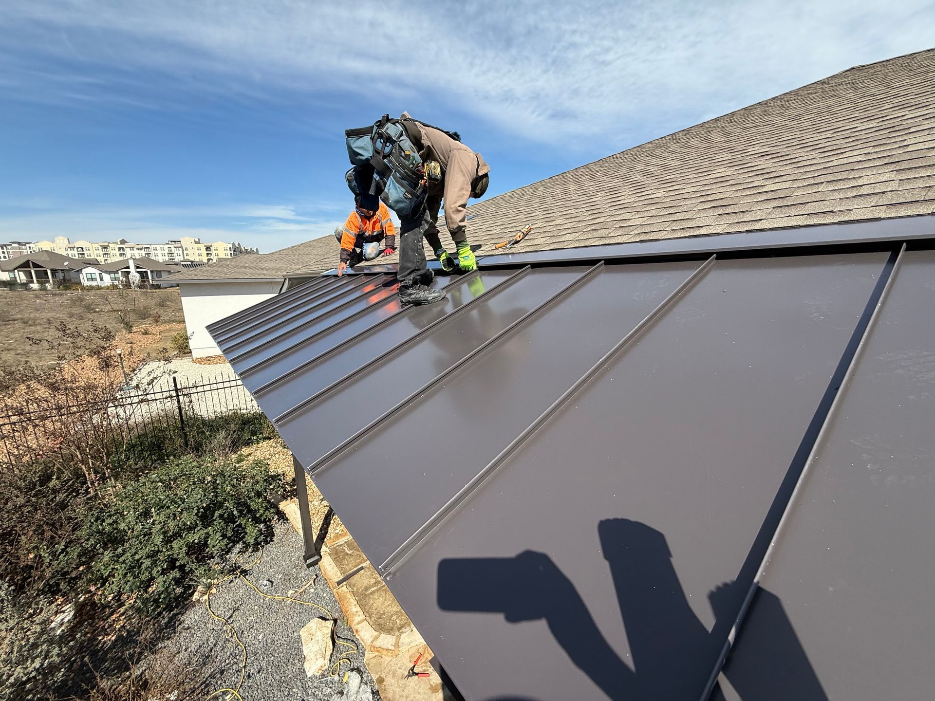 Roofer in safety harness installing a bracket on a shingled roof, holding a tool.