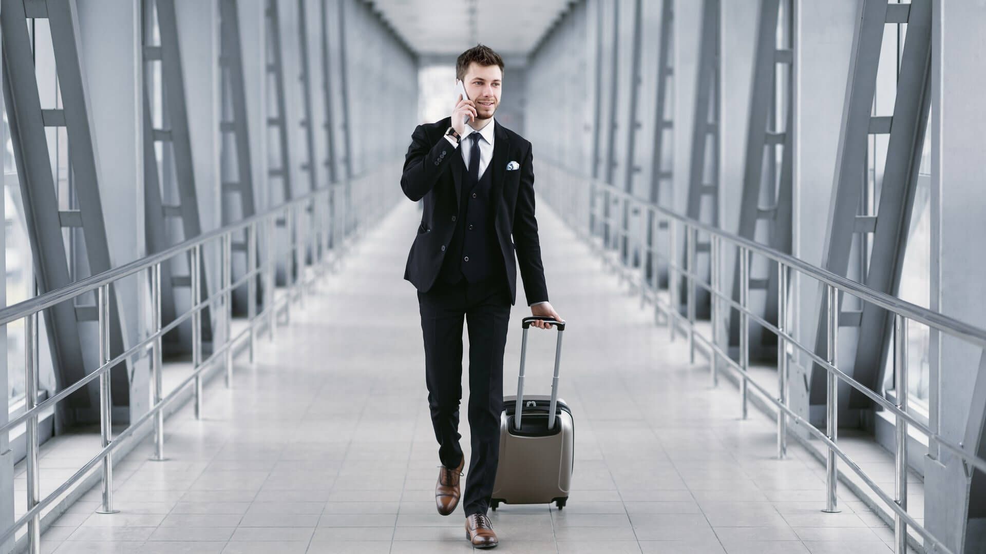 Urban business man in suit talking on smart phone traveling walking with luggage inside the airport, empty space