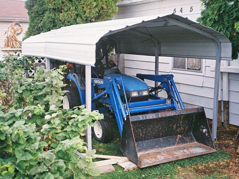 A blue tractor is parked under a white carport