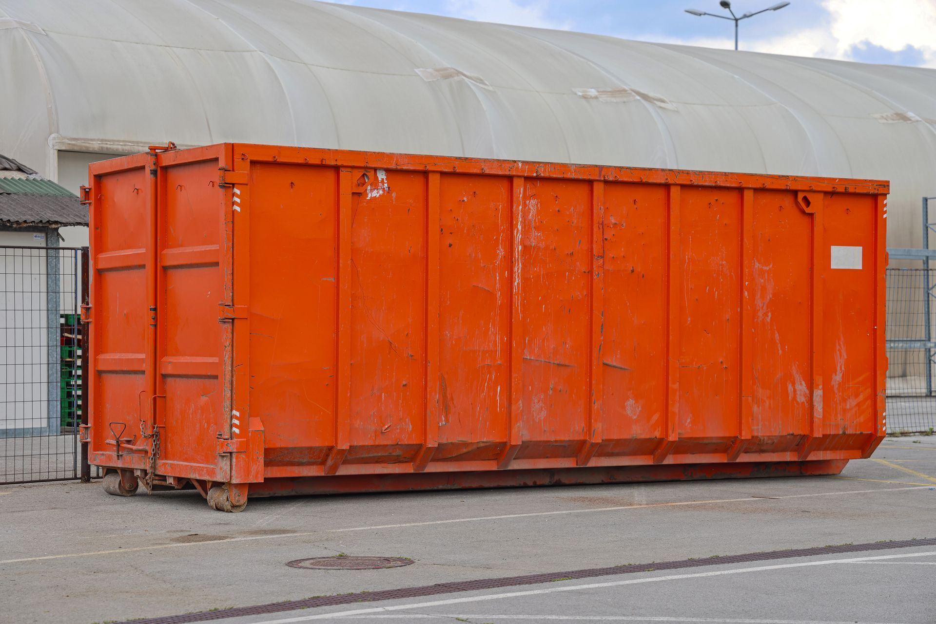 Large orange commercial roll off containers placed on concrete pavement near industrial facility.
