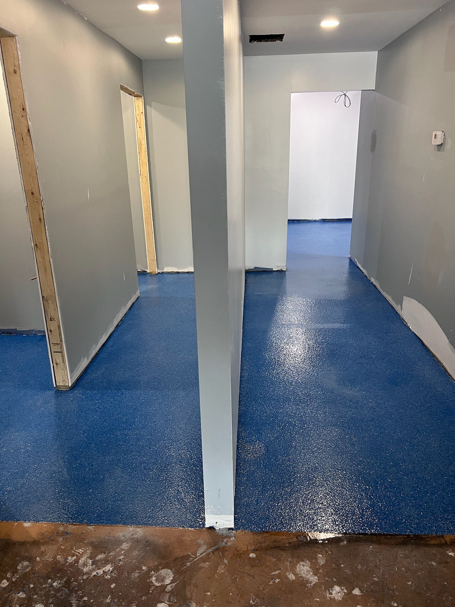 An interior shot shows a blue epoxy floor in a building under construction, with gray walls and a support beam.