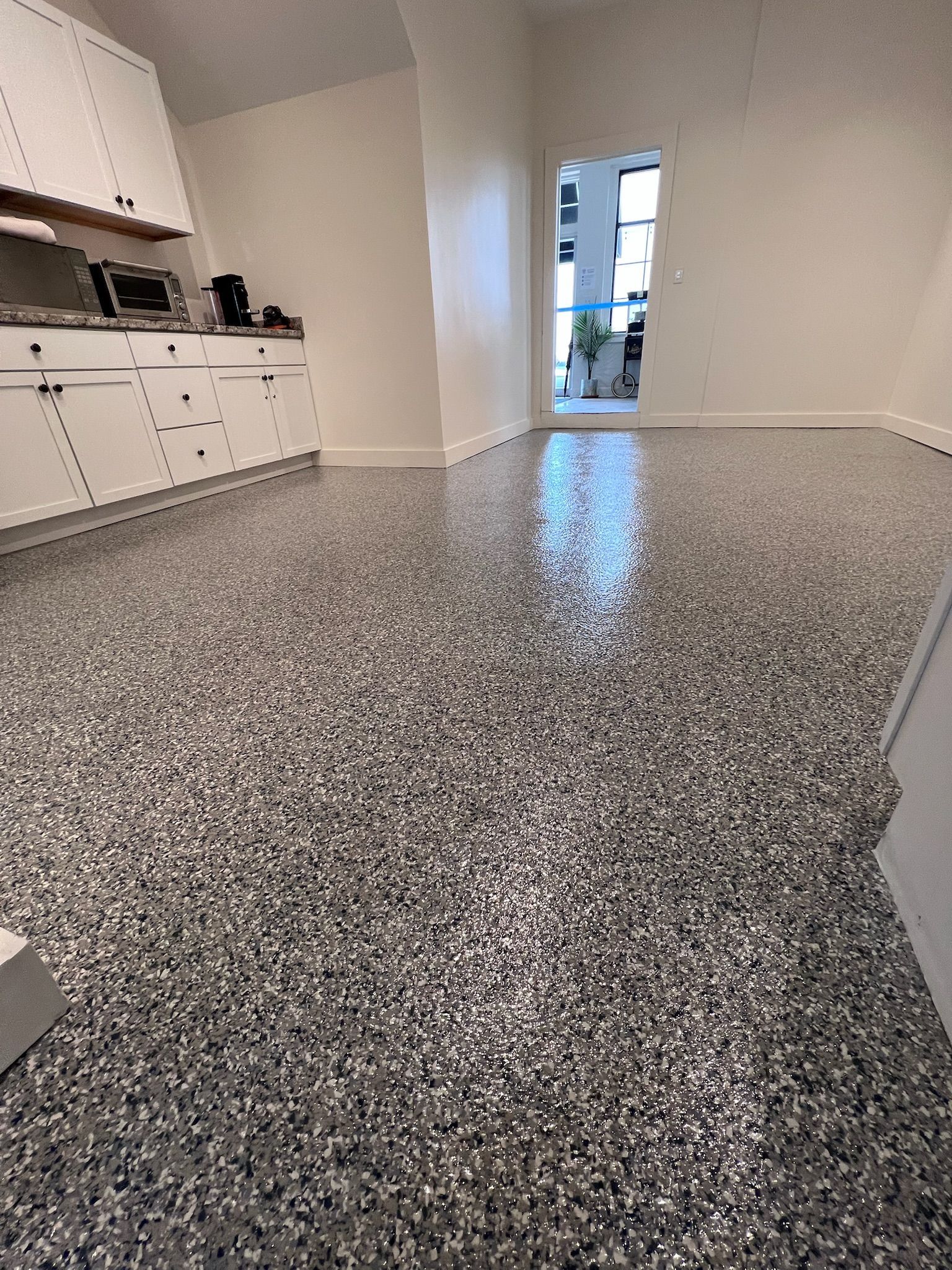 Gray flecked epoxy floor in a room with white cabinets and doorway.
