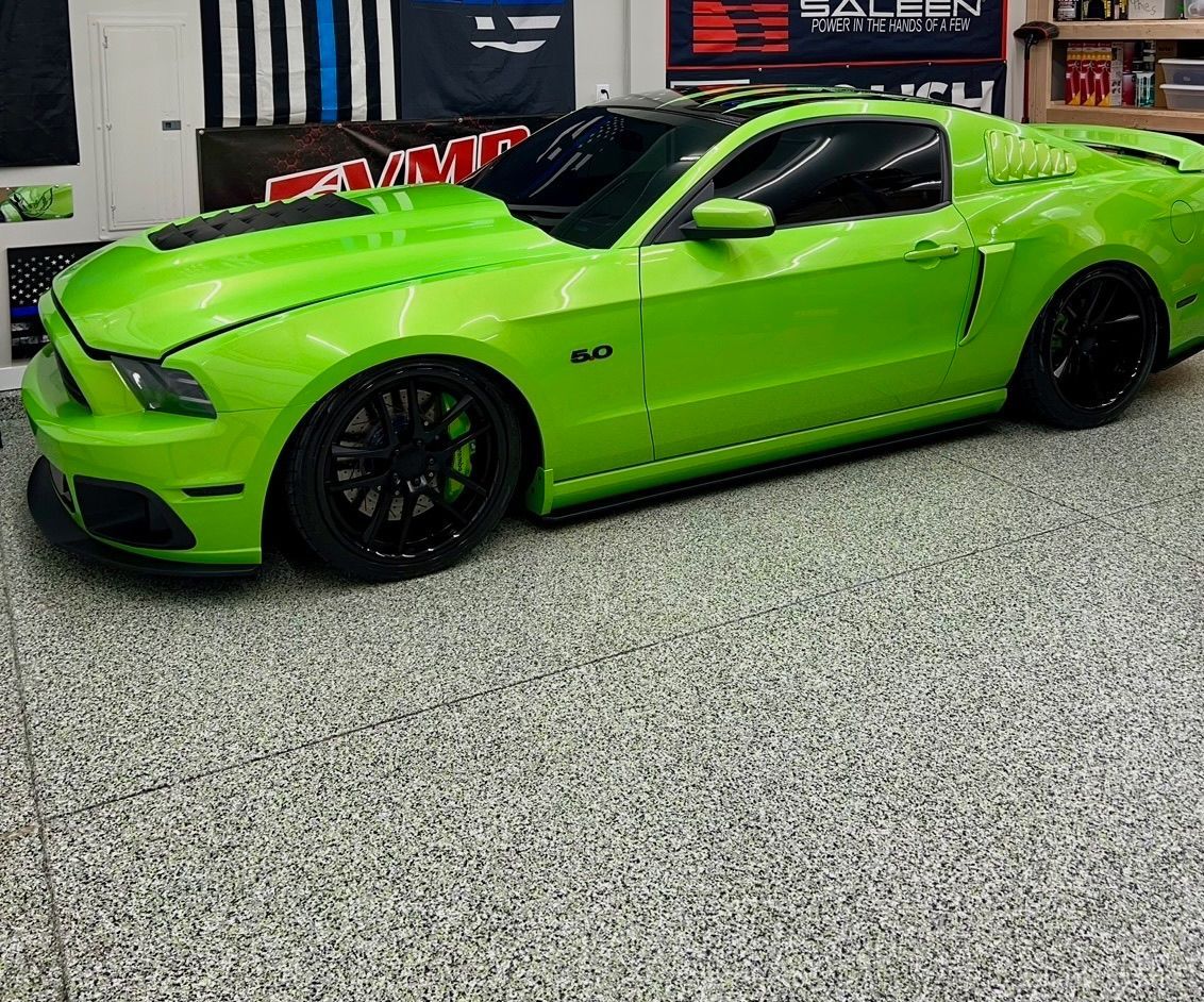 Green Ford Mustang with black wheels parked in a garage.