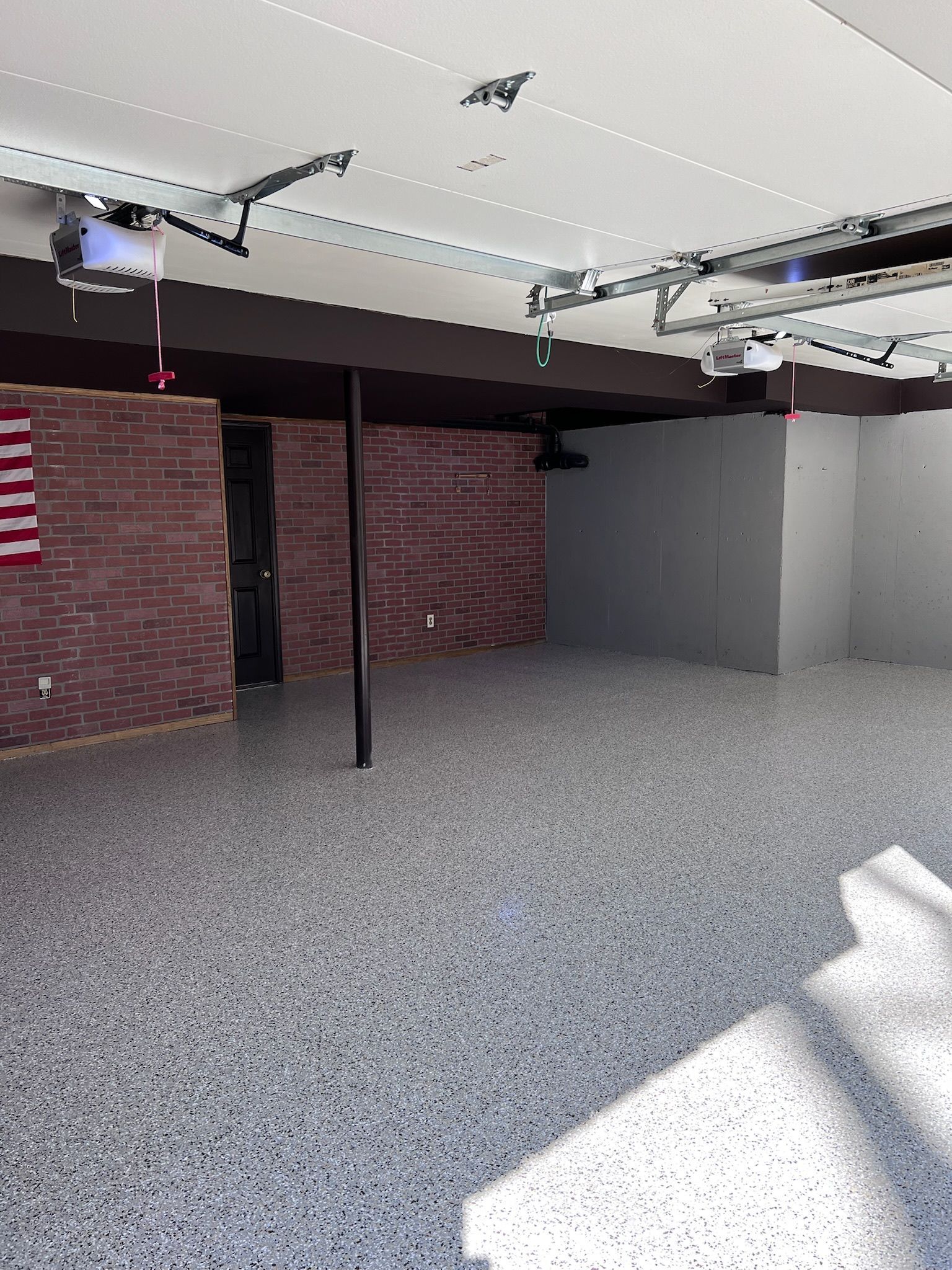 Empty garage interior with epoxy floor, exposed brick, and an American flag.