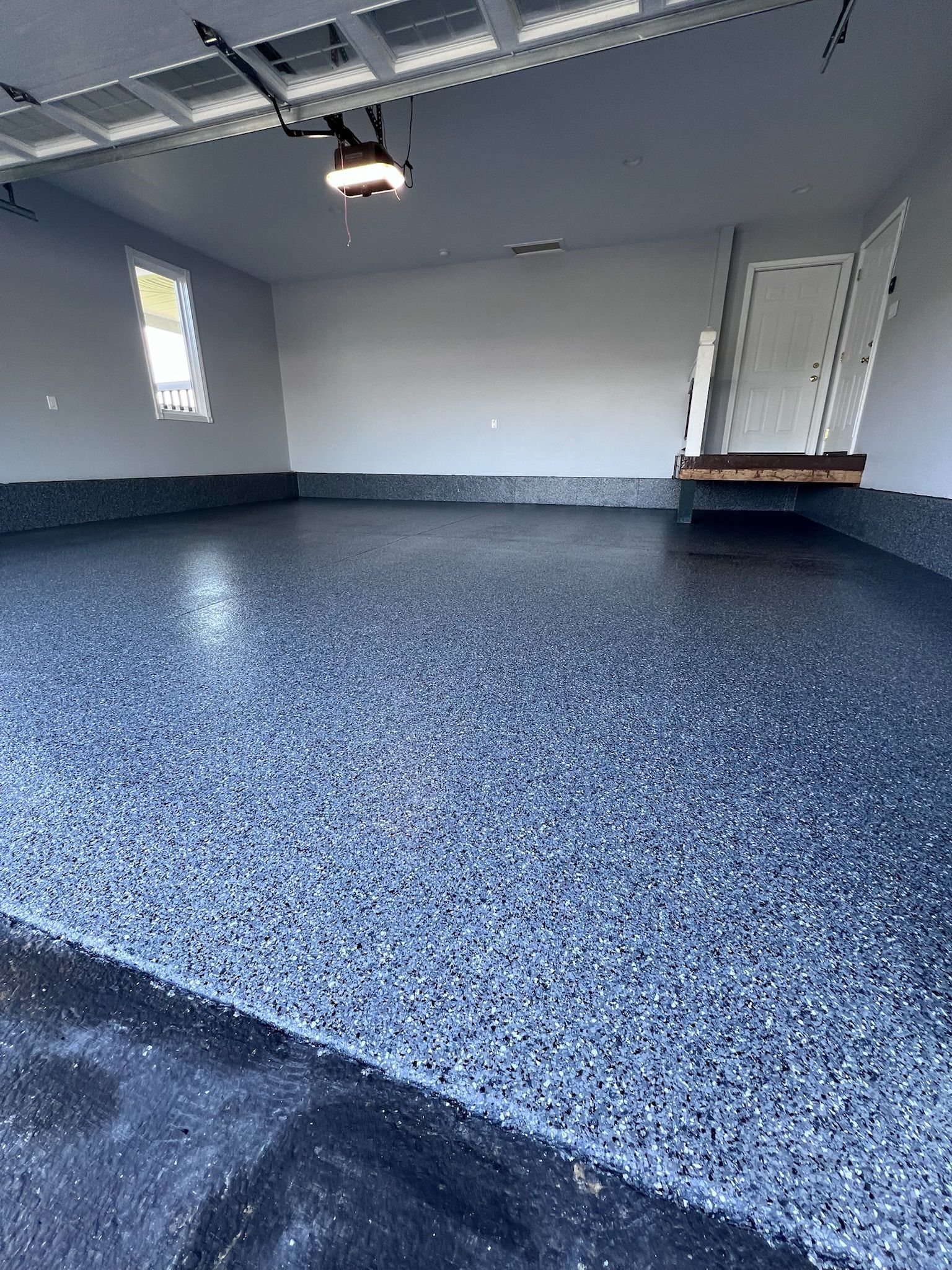 A garage interior with a speckled dark blue epoxy floor, light gray walls, and an open garage door.