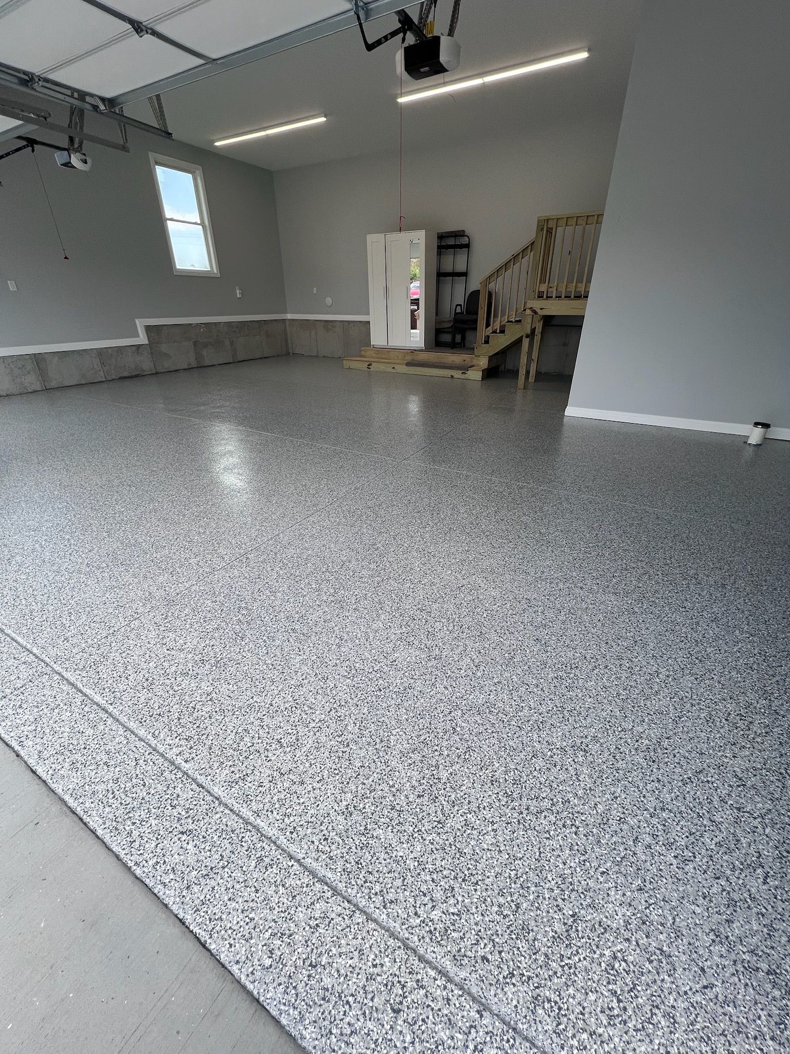 Garage interior with gray and white speckled epoxy floor, stairs, and a small window.