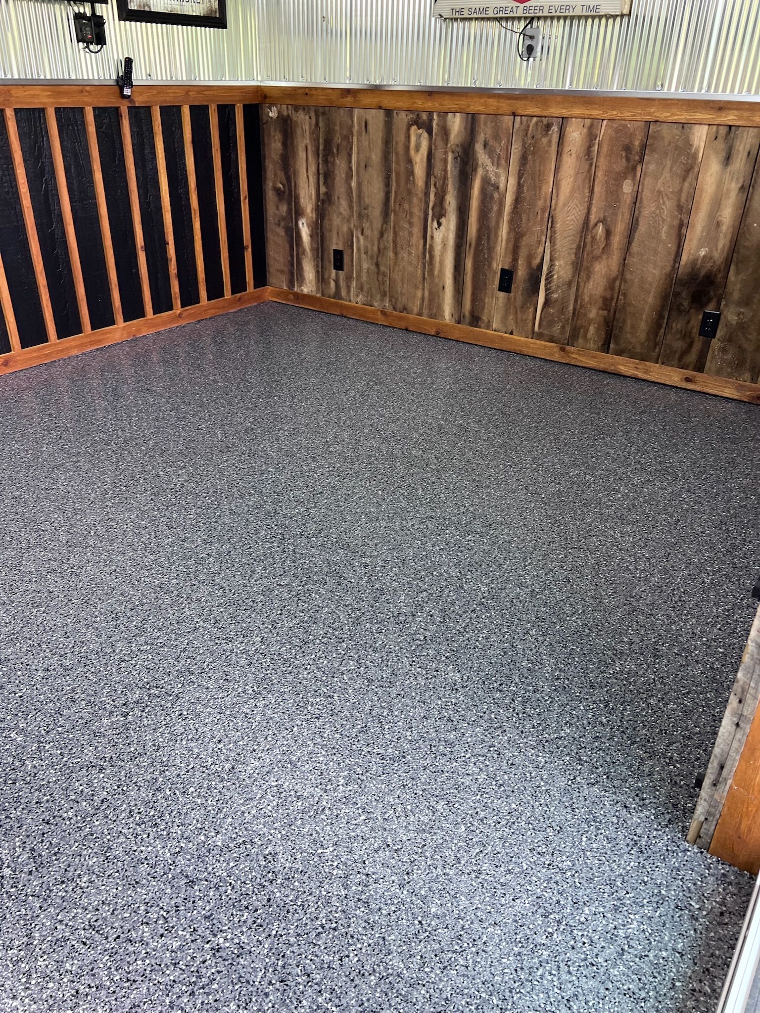 Room with gray speckled epoxy flooring, wood paneling walls, and black vertical stripes on a side wall.