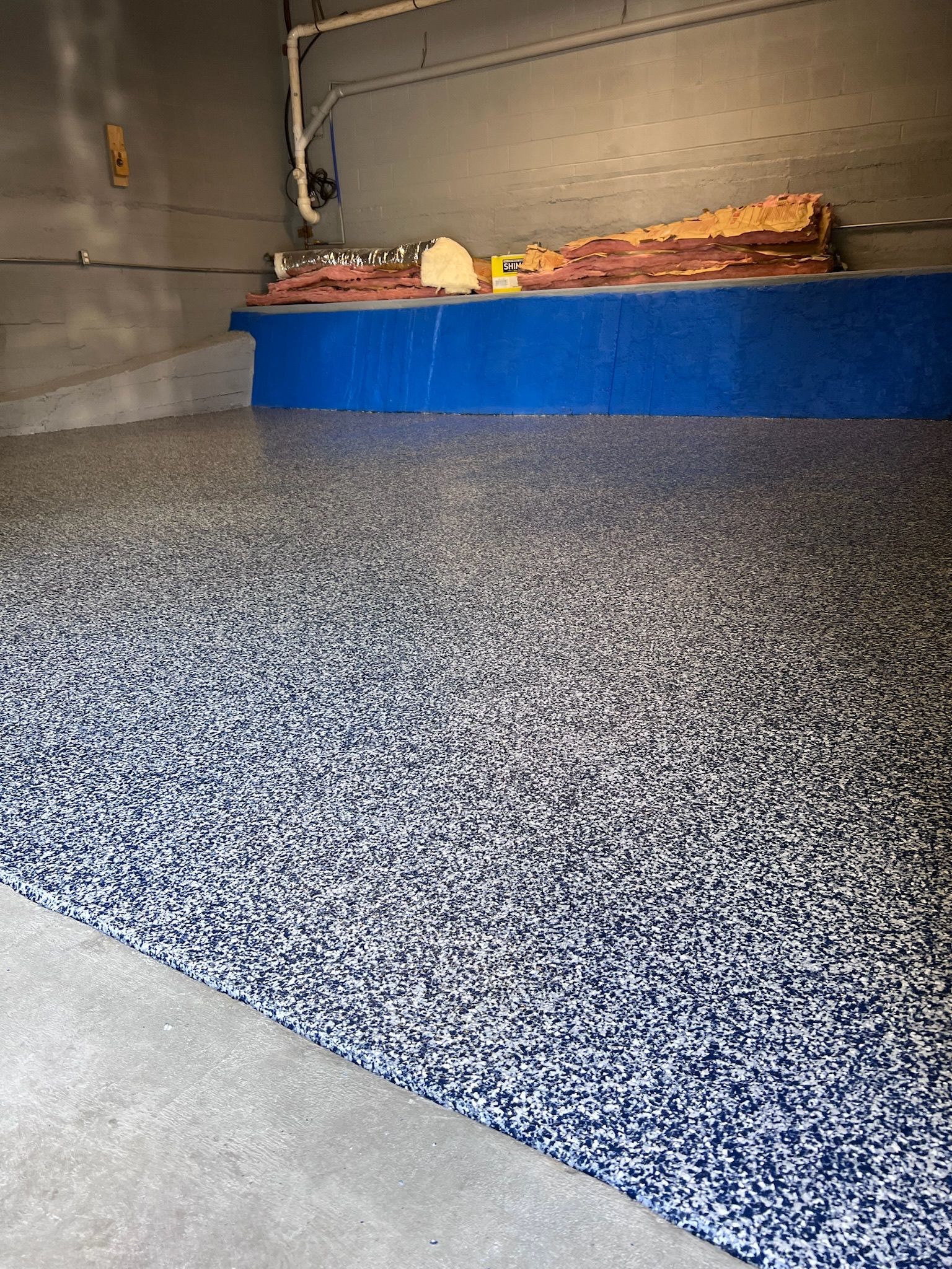Epoxy-coated garage floor with blue, white, and black flecks. Blue wall in the background with shelves.