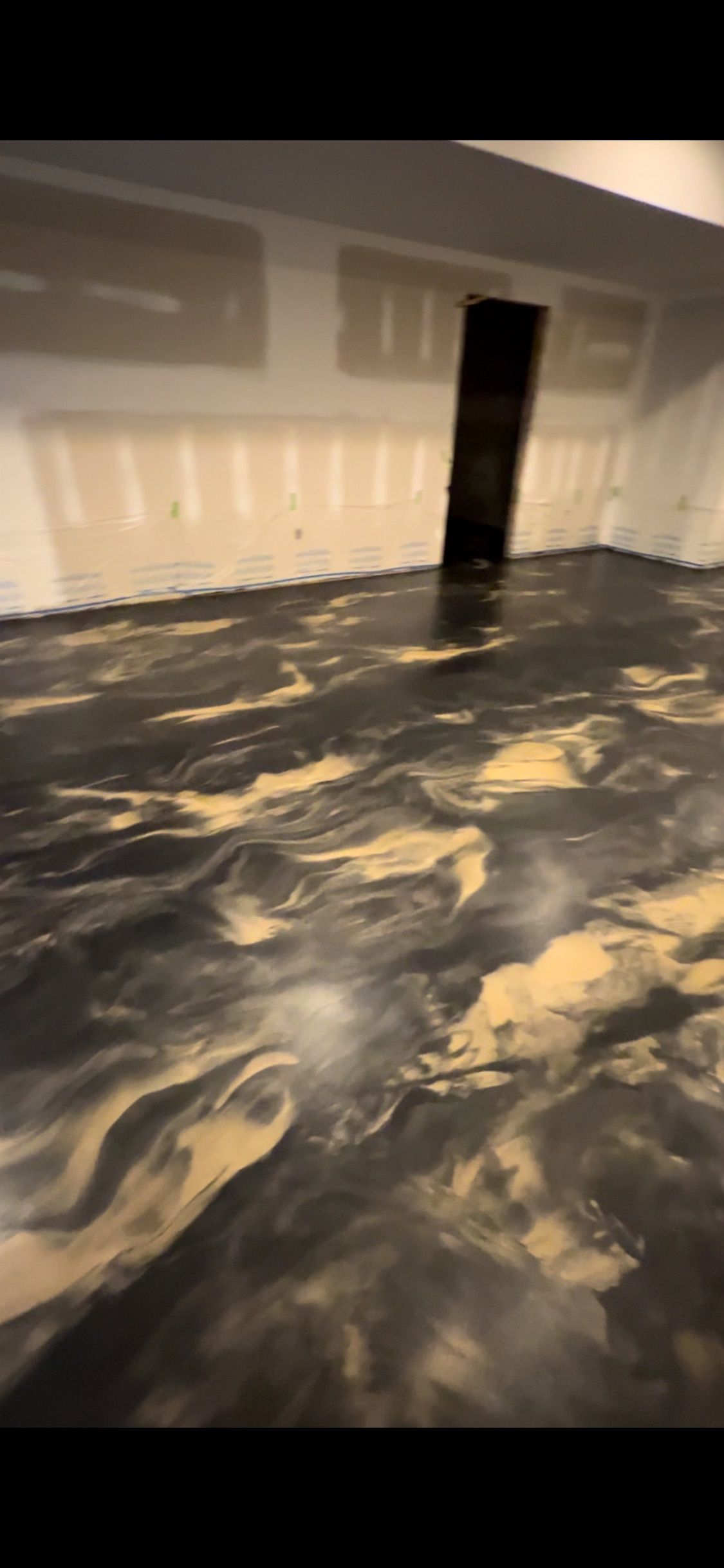A newly installed epoxy floor in a room, with dark gray and gold swirling patterns.
