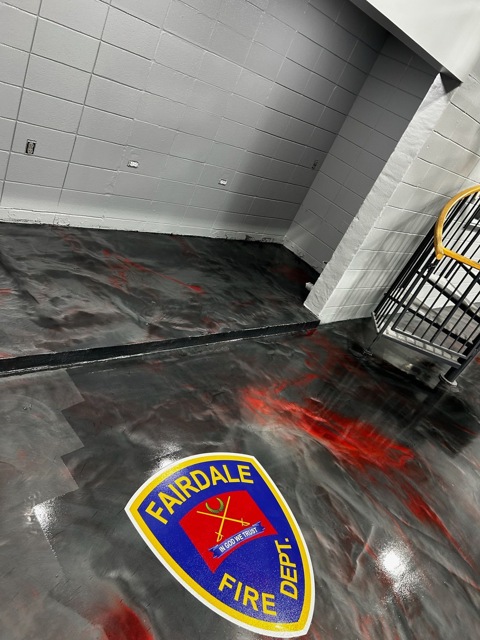 Fairdale Fire Dept. logo on a shiny, epoxy floor. Gray walls and a black metal cage in the corner. Red swirls visible.