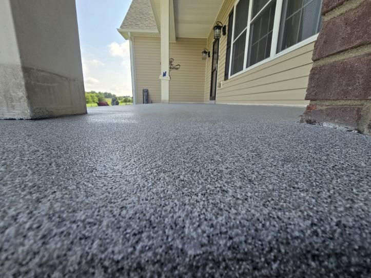 Close-up of a gray textured porch floor leading to a beige house with a porch and brick accents.