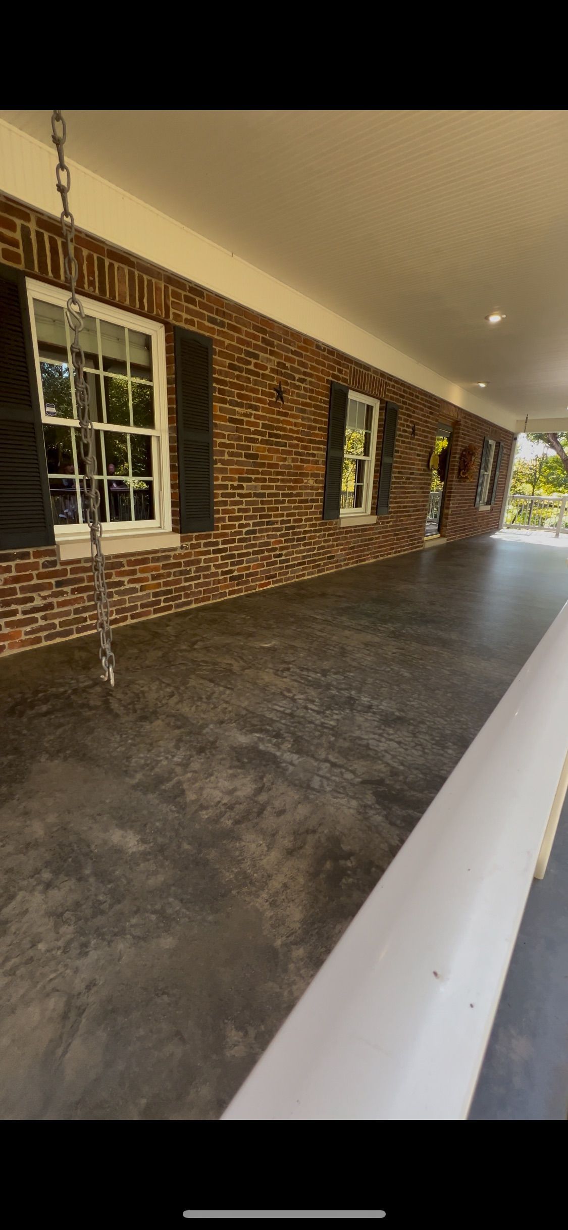 Covered porch with brick wall, windows, and dark flooring.