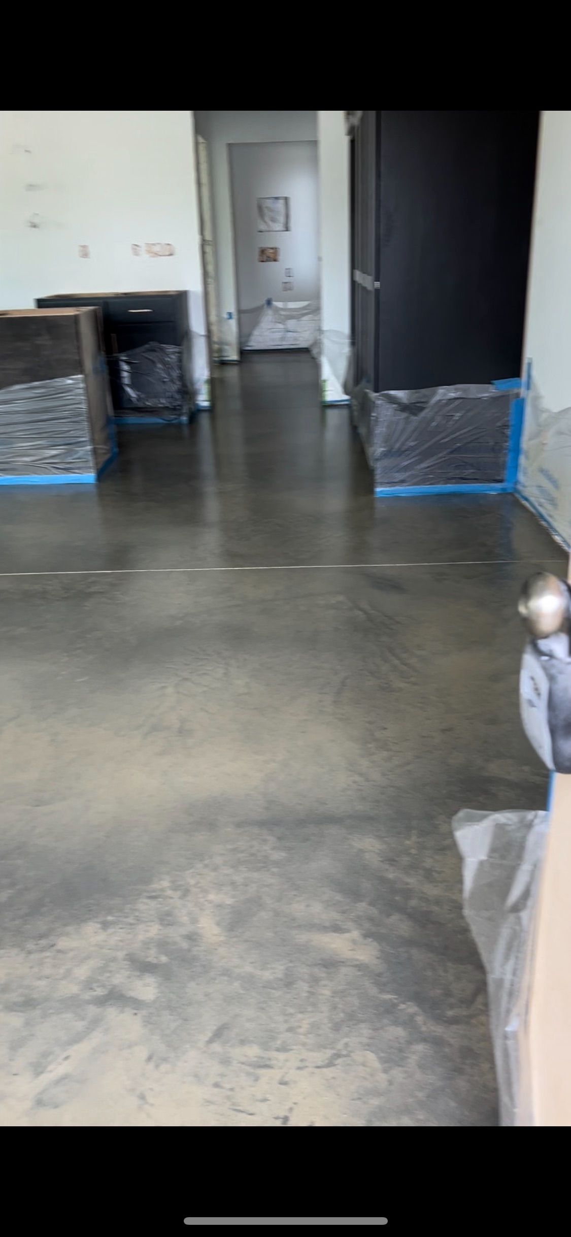 A room with a polished gray concrete floor, leading to a bathroom. Cabinets are covered in plastic.
