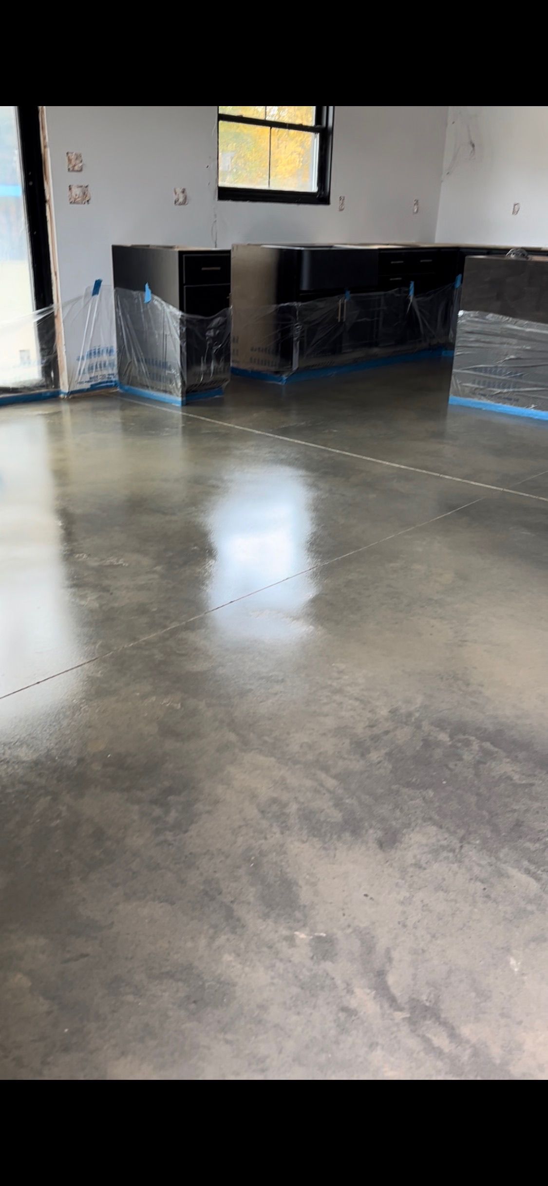 Kitchen interior with polished concrete floor, black cabinets, and a window.